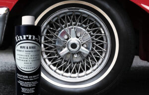 Tarn-X cleaner bottle in front of a shiny wire-spoke car wheel with a whitewall tire.