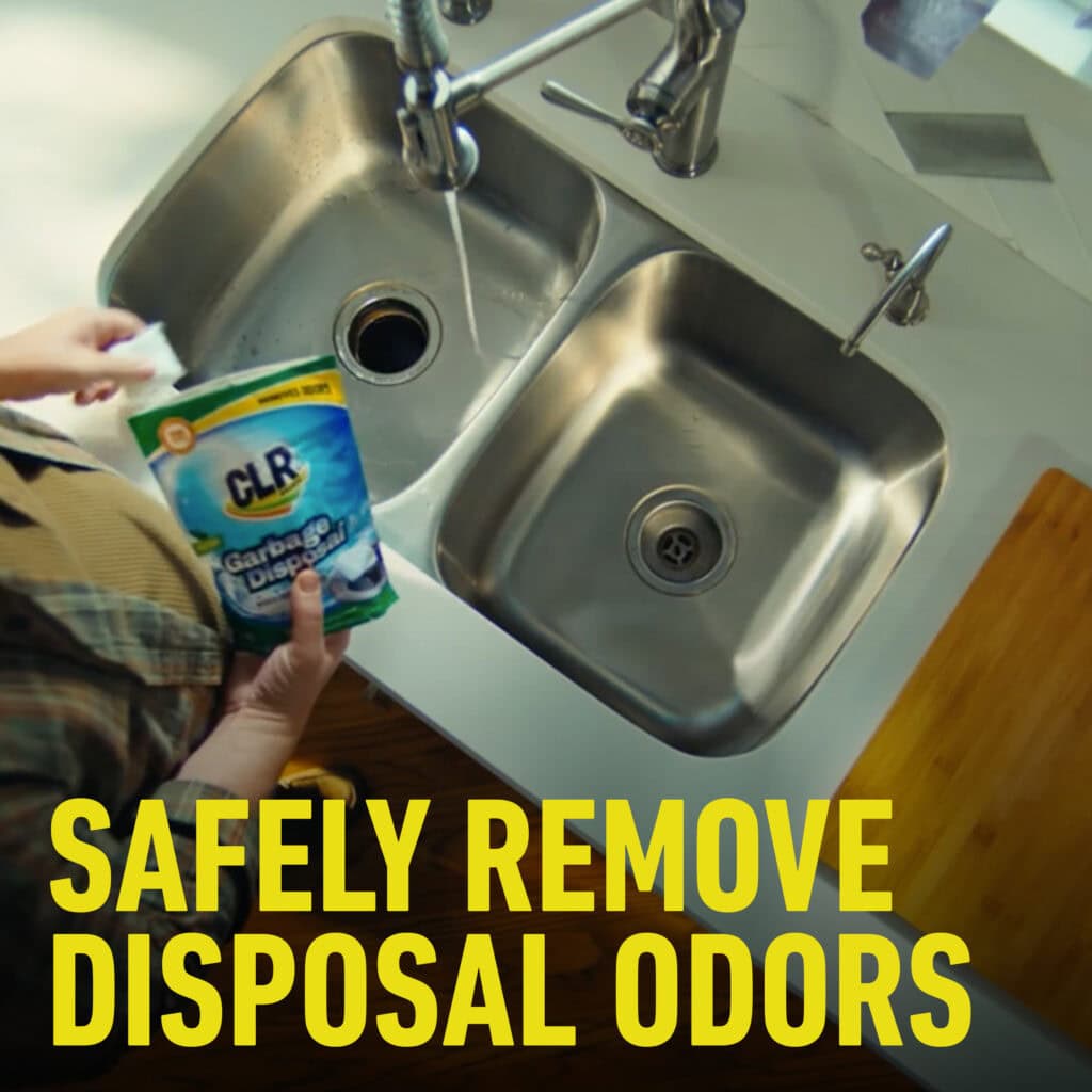 Person holds CLR Garbage Disposal Cleaner pouch over kitchen sink, bold text: Safely Remove Disposal Odors.