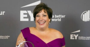 Smiling woman in purple dress holds award in front of EY and Building a better working world backdrop.