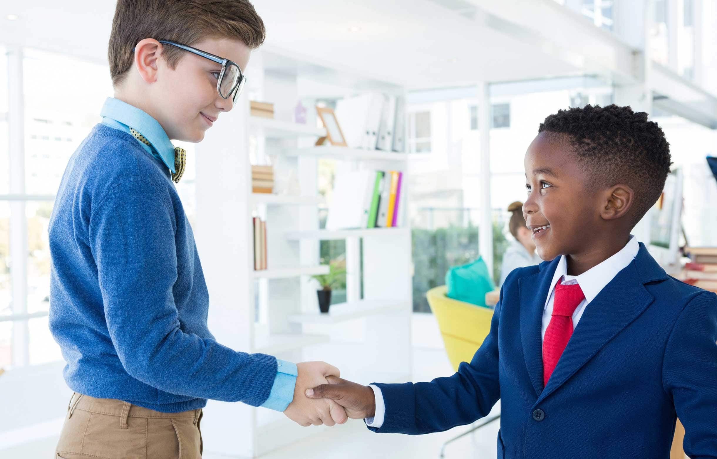 Two young boys in suits shaking hands.