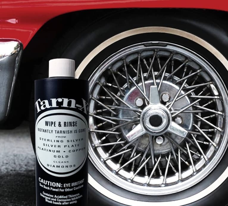Tarn-X cleaner bottle in front of a classic car’s wire-spoke wheel and red fender.