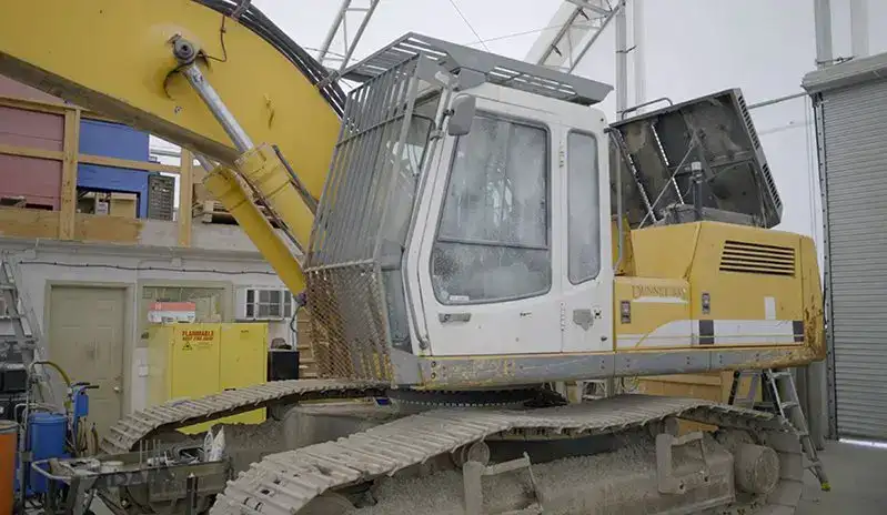 Yellow excavator indoors with open engine compartment and metal safety cage around cab.