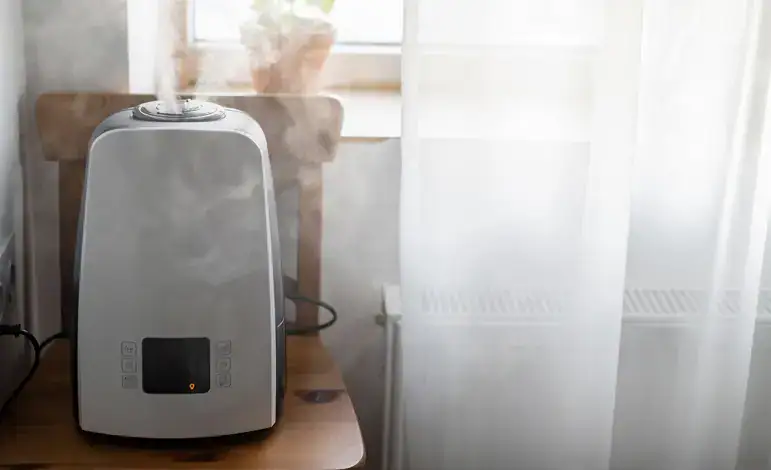 Humidifier with visible mist on wooden chair near window with sheer curtains; plant in background.